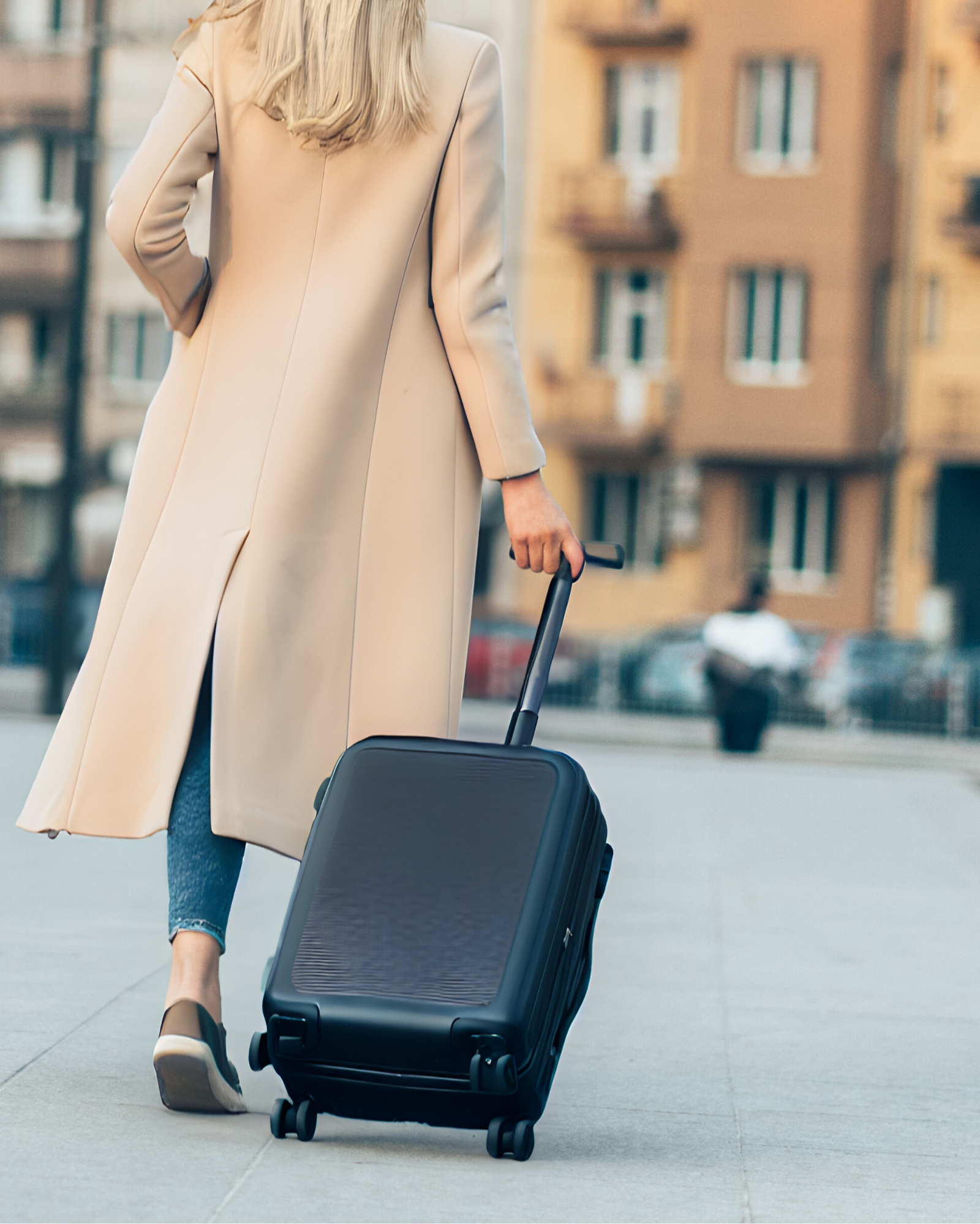 Blonde woman walking down the street, pulling a suitcase behind her.